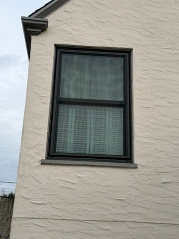 Black aluminum double-hung window on white stucco exterior, East Bay