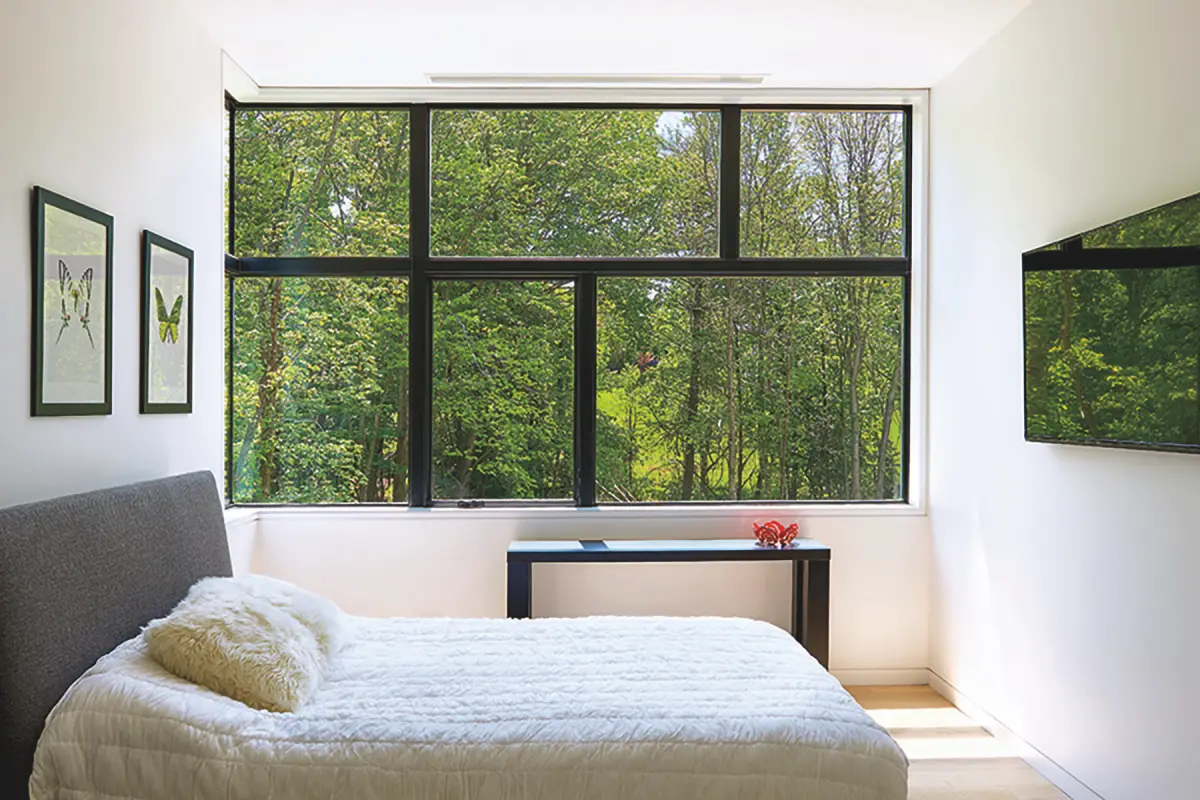 Bedroom with large dark-framed windows facing trees