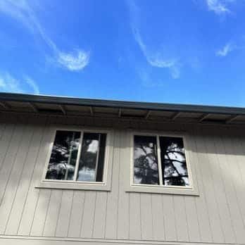 Two new vinyl windows on gray home exterior with blue sky, East Bay