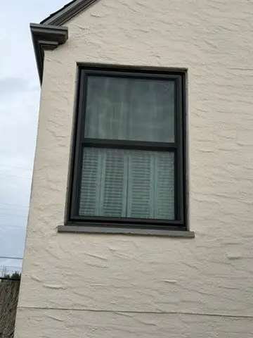 Black aluminum double-hung window on white stucco exterior, East Bay